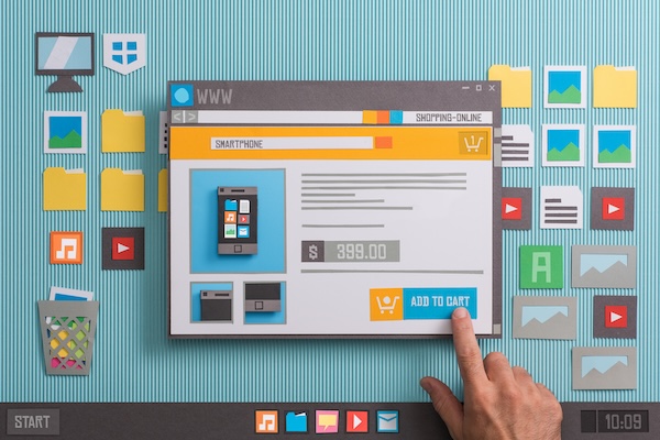 A finger hovers over an "add to cart" button on an online shopping website, designed as paper craft. The scene depicts the digital realm of e-commerce, with website windows, files, music notes, and other icons scattered on a simulated desktop interface.