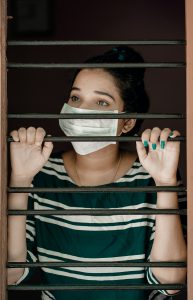A woman behind security bars wearing a medical mask