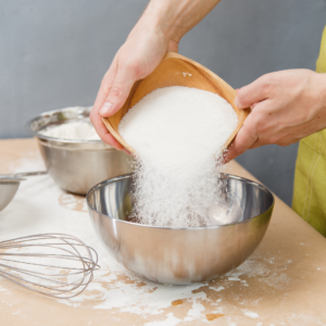 A baker pouring sugar into a steel bowl