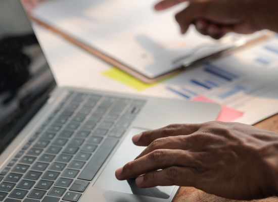 someone working on a laptop on a desk scattered with a lot of business, website, and marketing related documents.