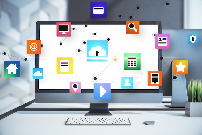 A modern monitor displays colourful graphic icons on a white desk, with a keyboard and mouse nearby. The digital icons appear to be floating on the screen.