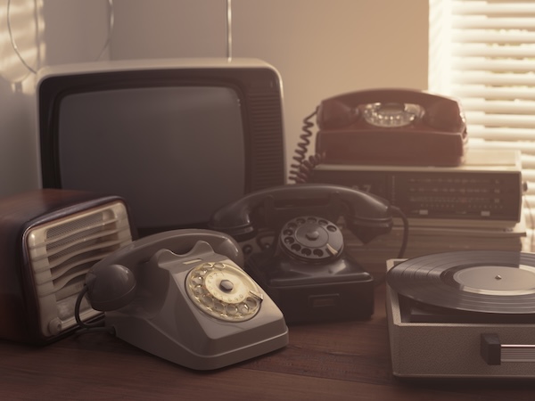 Vintage retro revival objects and second-hand appliances collection on a table: record player, television, radio and rotary dial telephones.