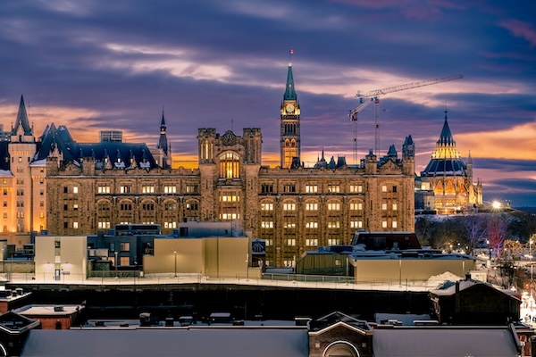 A sprawling cityscape at night, showcasing the Canadian Parliament Buildings in Ottawa, Ontario. The scene is bathed in the soft, ambient glow of nighttime lighting, with multiple windows illuminated across the building facades.